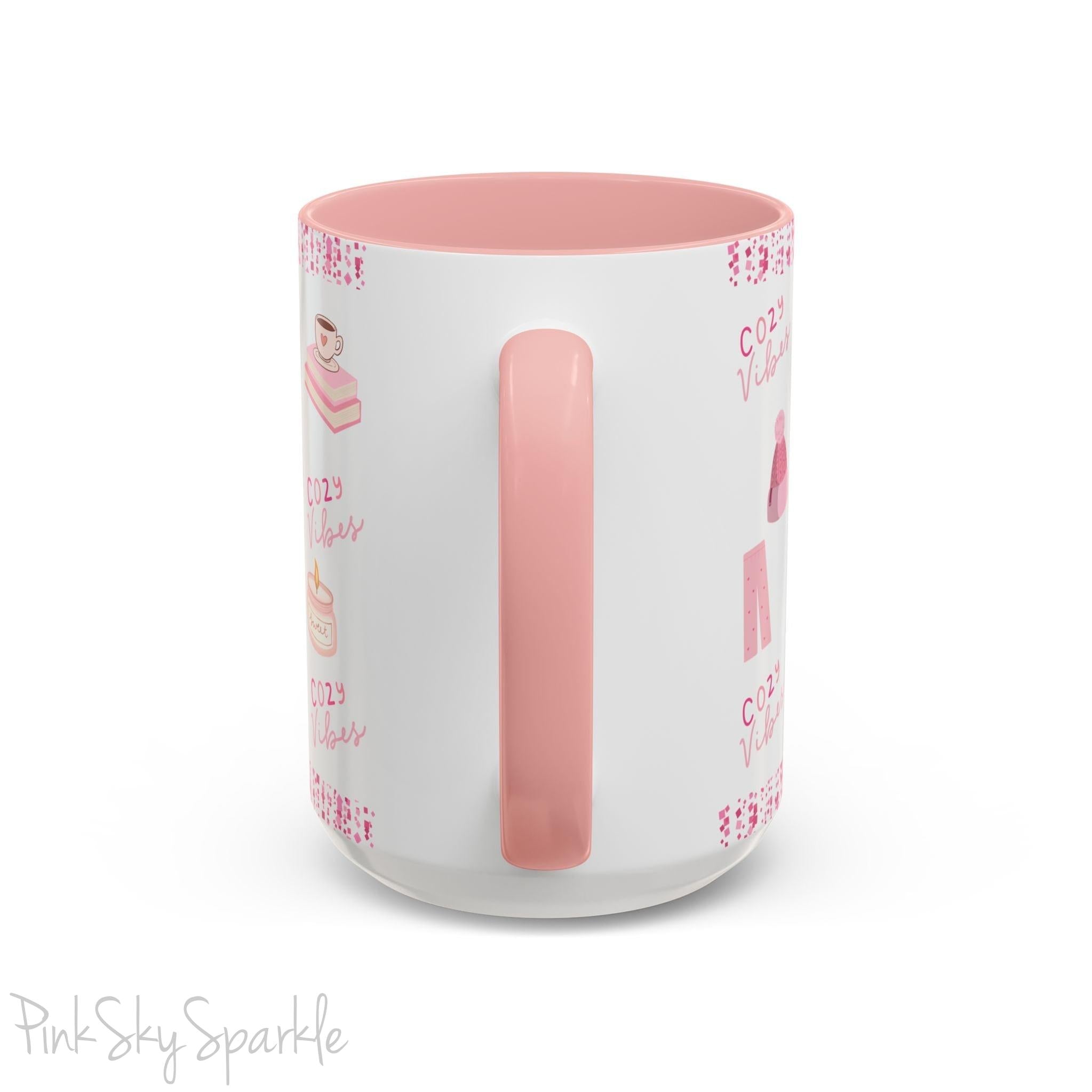 Pink Cozy Vibes Mug - Perfect for coffee, tea, or hot cocoa lovers! This ceramic mug features 'cozy vibes' in a pink font, surrounded by cute illustrations of pink cozy items such as slippers, mittens, blankets and candles. Ideal for creating a warm, cozy atmosphere, this pink-handled mug (also available in light blue, black and navy) makes a great gift for anyone who loves comfort, style and the color pink.