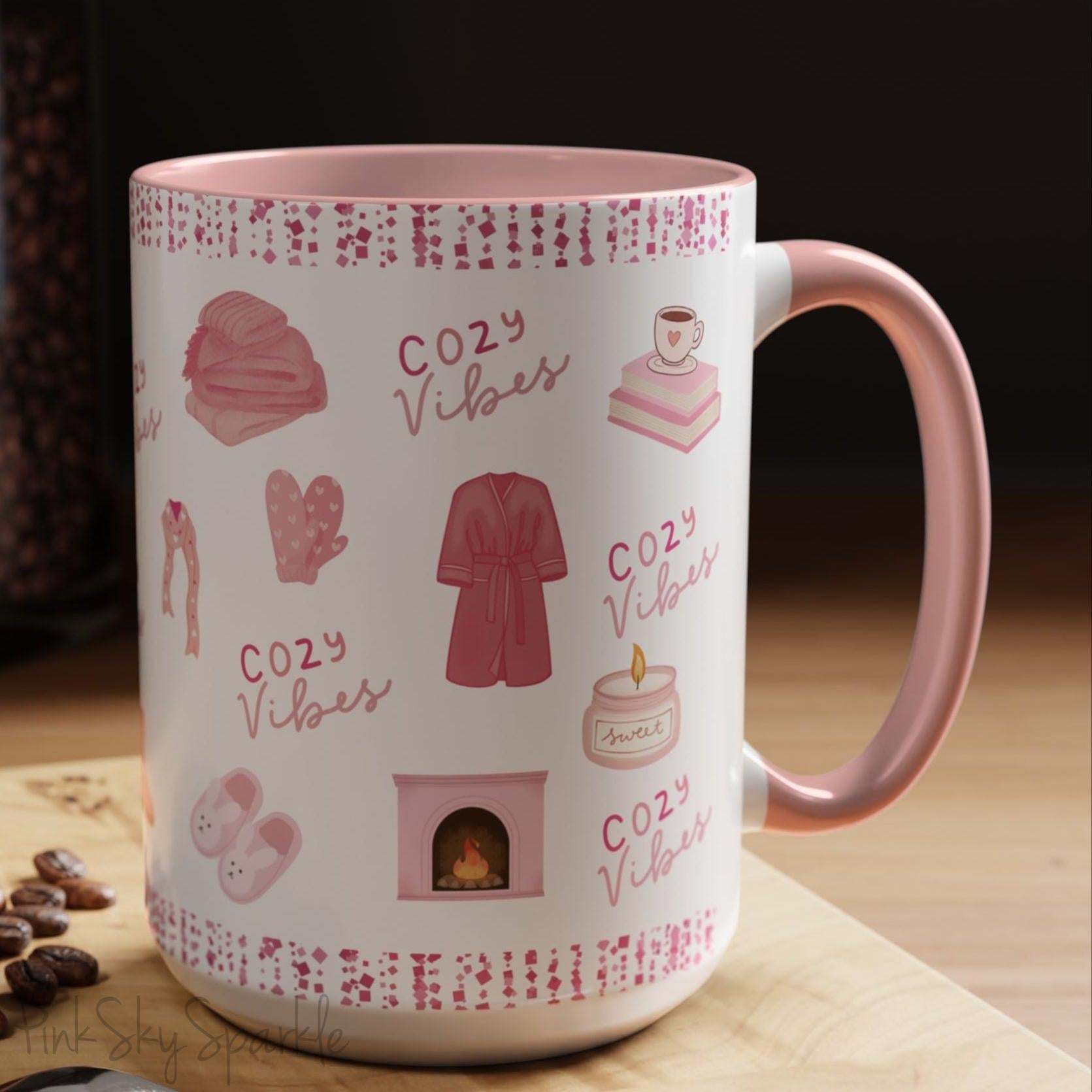 Pink Cozy Vibes Mug - Perfect for coffee, tea, or hot cocoa lovers! This ceramic mug features 'cozy vibes' in a pink font, surrounded by cute illustrations of pink cozy items such as slippers, mittens, blankets and candles. Ideal for creating a warm, cozy atmosphere, this pink-handled mug (also available in light blue, black and navy) makes a great gift for anyone who loves comfort, style and the color pink.