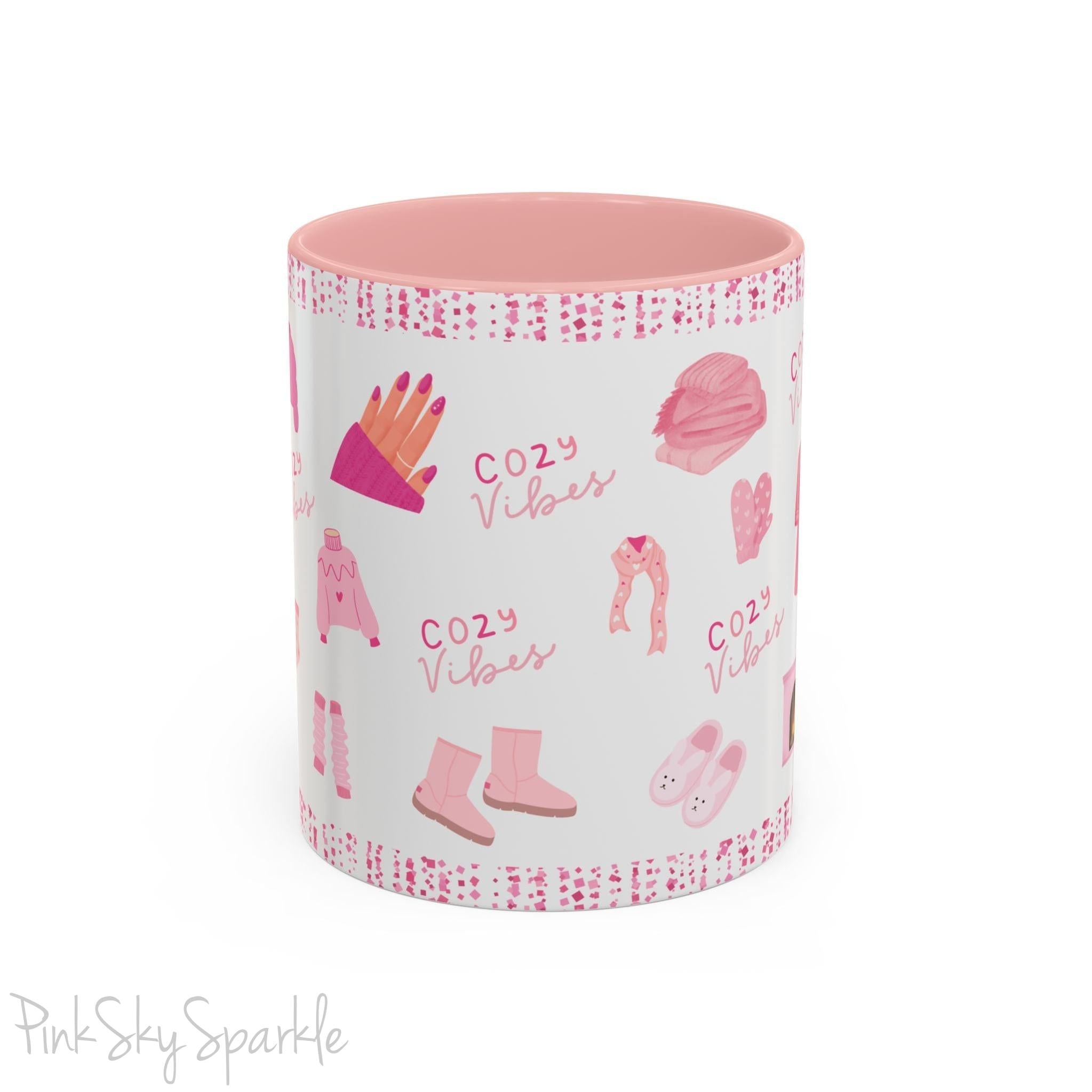 Pink Cozy Vibes Mug - Perfect for coffee, tea, or hot cocoa lovers! This ceramic mug features 'cozy vibes' in a pink font, surrounded by cute illustrations of pink cozy items such as slippers, mittens, blankets and candles. Ideal for creating a warm, cozy atmosphere, this pink-handled mug (also available in light blue, black and navy) makes a great gift for anyone who loves comfort, style and the color pink.