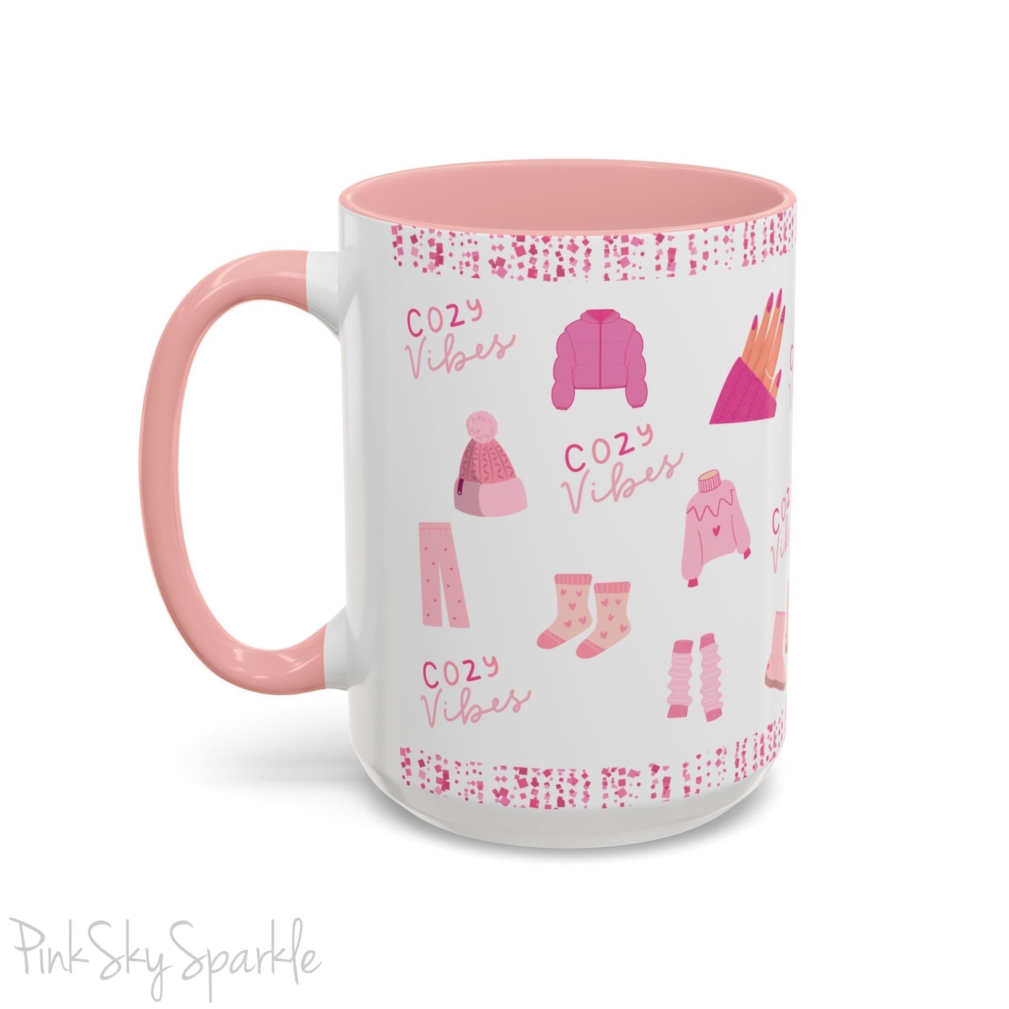 Pink Cozy Vibes Mug - Perfect for coffee, tea, or hot cocoa lovers! This ceramic mug features 'cozy vibes' in a pink font, surrounded by cute illustrations of pink cozy items such as slippers, mittens, blankets and candles. Ideal for creating a warm, cozy atmosphere, this pink-handled mug (also available in light blue, black and navy) makes a great gift for anyone who loves comfort, style and the color pink.