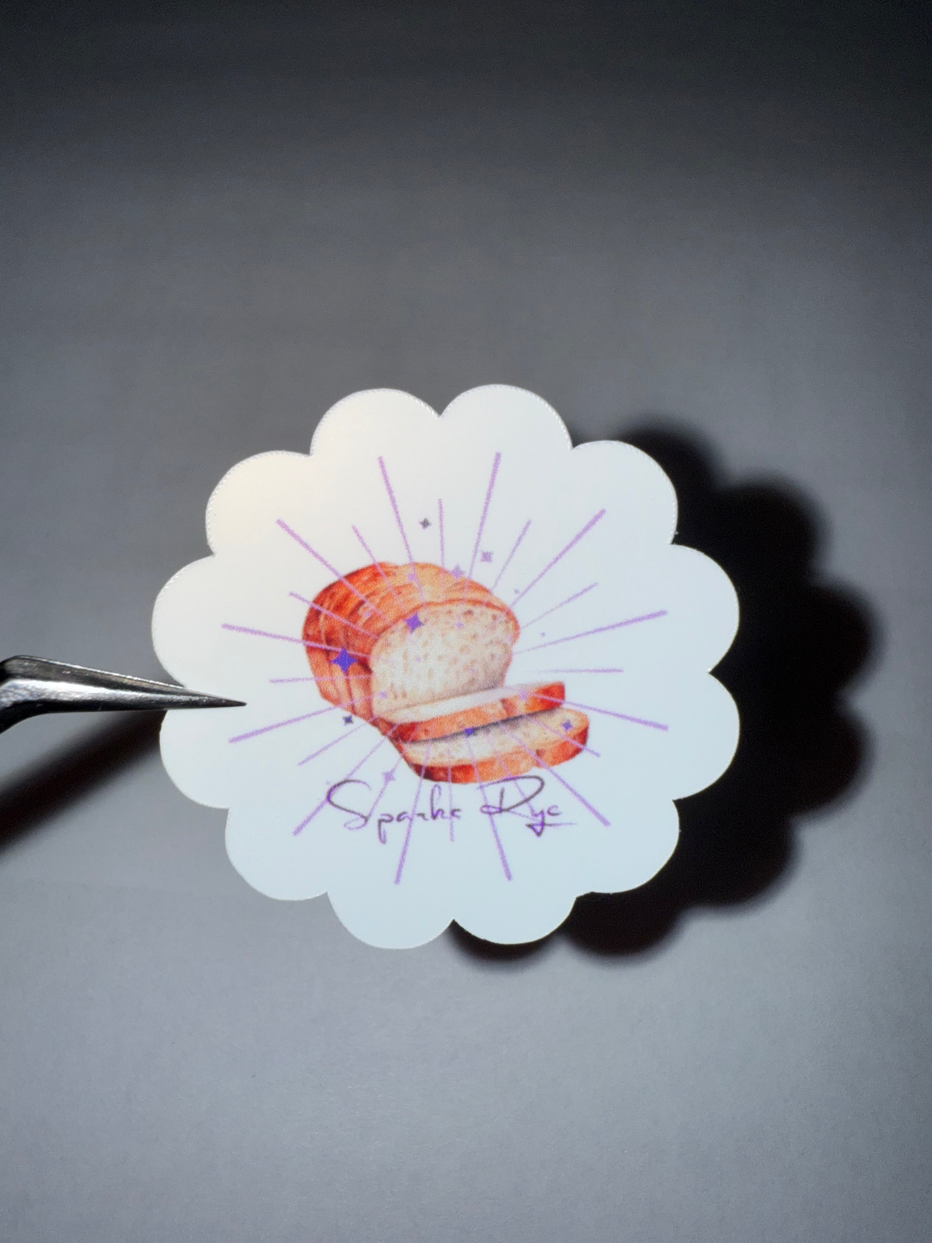 Flower shaped sticker with a loaf of bread and purple sparks and stars with the words "Sparks Rye".
