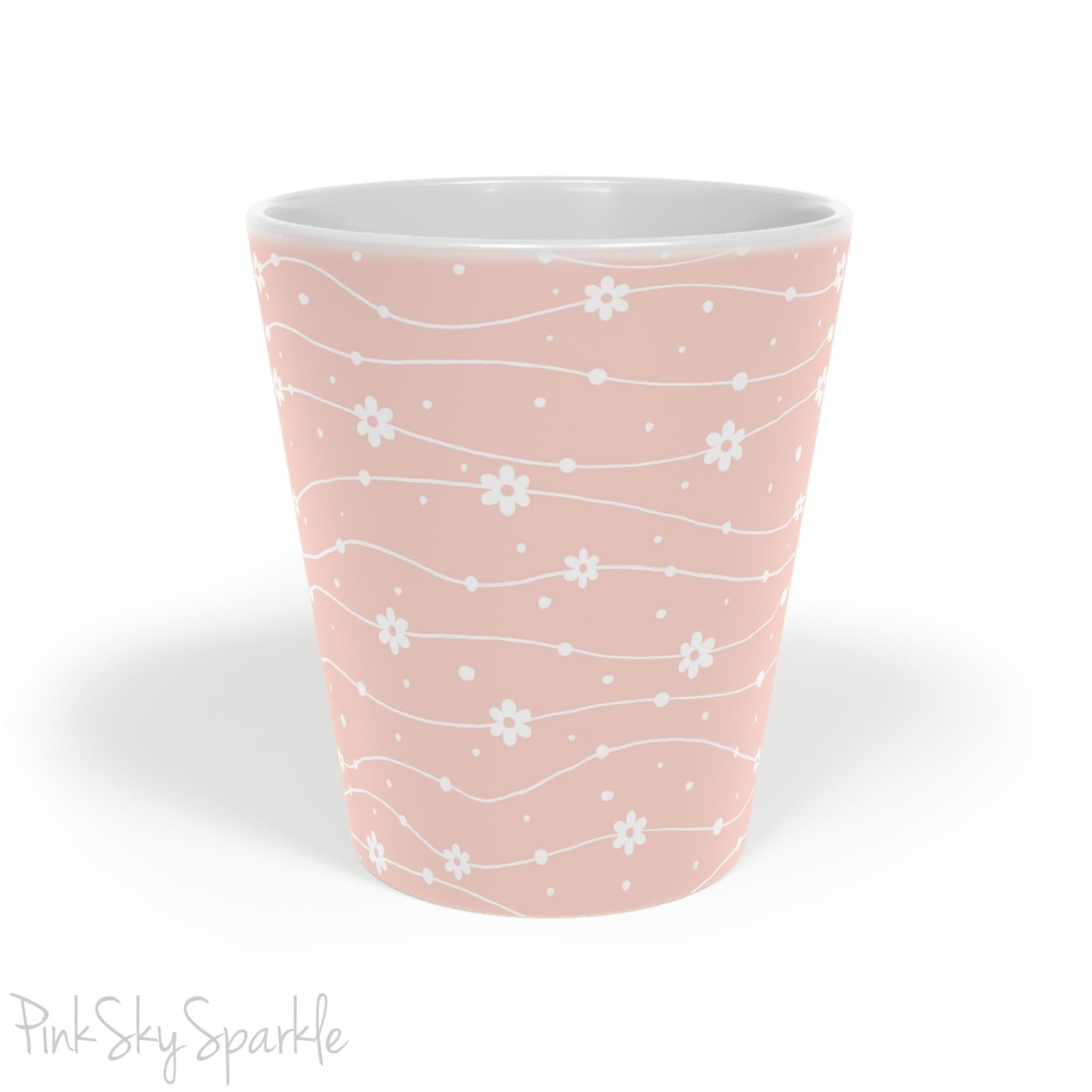 Experience the joy of sipping your favourite latte from our beautiful Wavy Daisy Latte Mug. Crafted from durable materials, this 12oz mug is perfect for everyday use and makes a lovely gift for any coffee or tea lover. Featuring a soft pink background on a white mug, with a wavy line pattern with white daisy flowers and dots throughout.