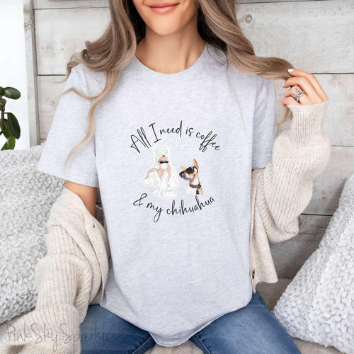 "All I need is coffee and my chihuahua" T-shirt. Featuring a graphic of a woman wearing a robe and hair towel, wearing black sunglasses drinking a coffee next to a chihuahua wearing black sunglasses.