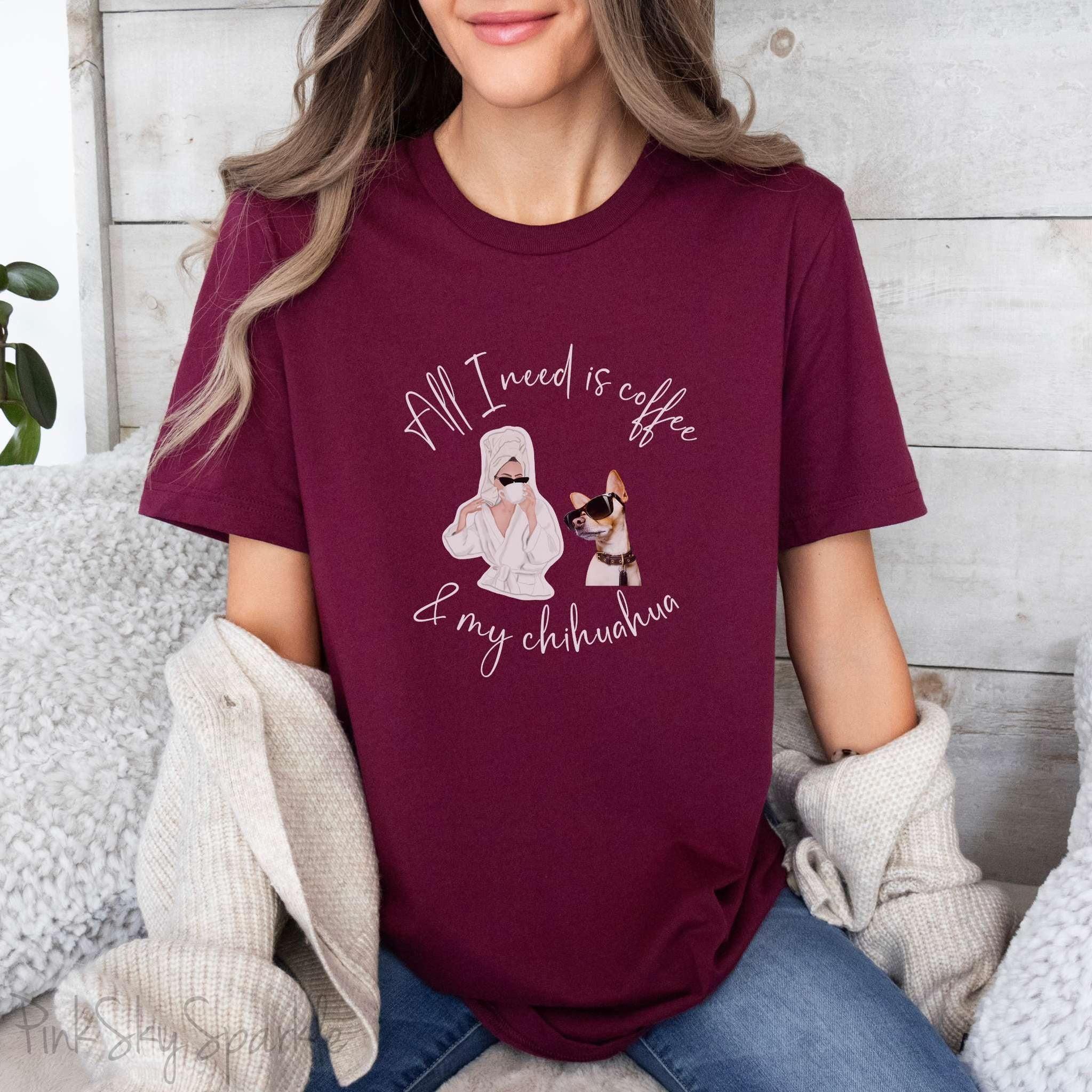 "All I need is coffee and my chihuahua" T-shirt. Featuring a graphic of a woman wearing a robe and hair towel, wearing black sunglasses drinking a coffee next to a chihuahua wearing black sunglasses.