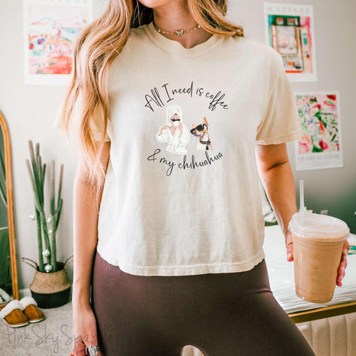"All I need is coffee and my chihuahua" Women's Boxy Tee. Featuring a graphic of a woman wearing a robe and hair towel, wearing black sunglasses drinking a coffee next to a chihuahua wearing black sunglasses.