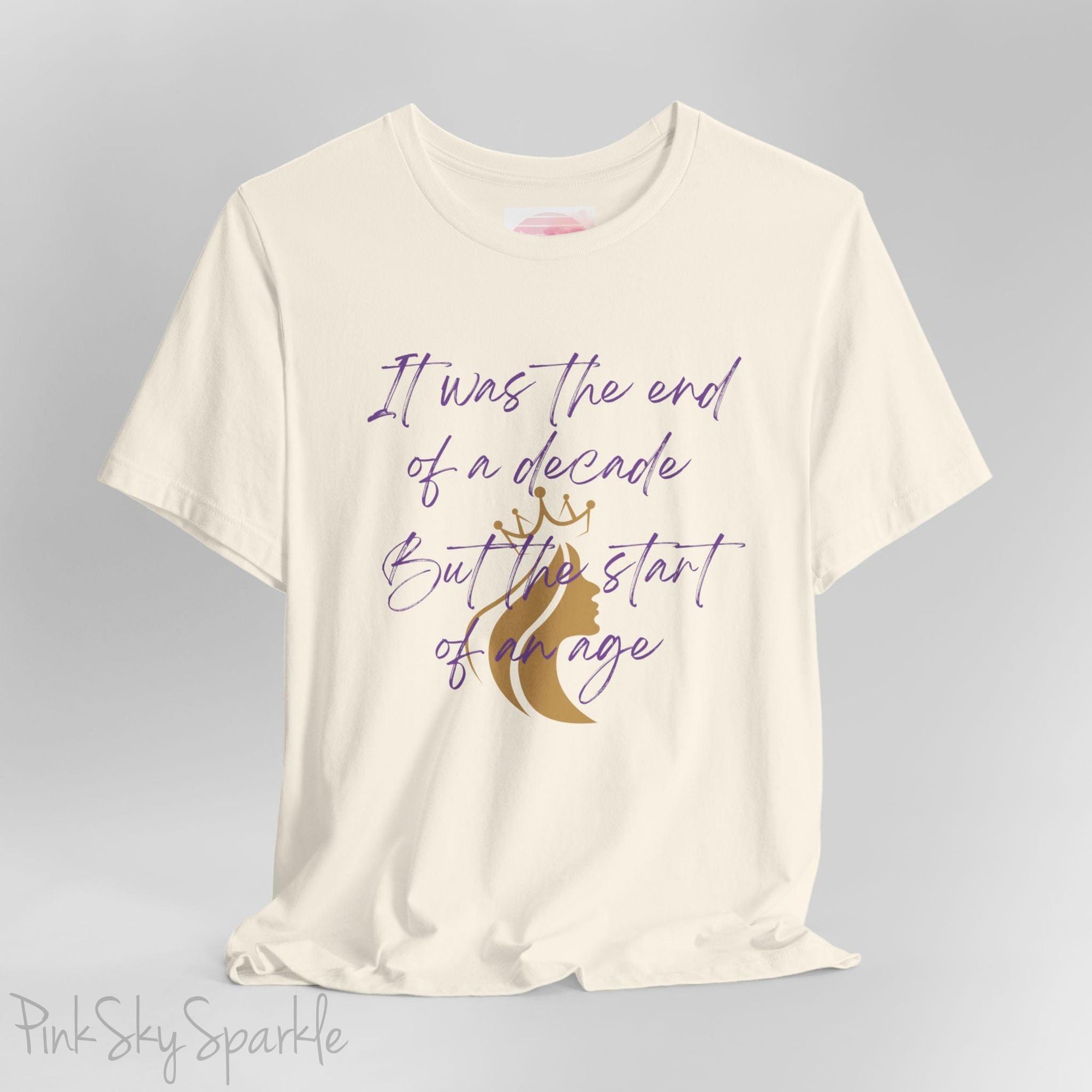 Embrace the excitement of a new era with our End of a Decade, Start of an Age T-shirt, inspired by Taylor Swift's iconic lyrics. Featuring the words It was the end of a decade, But the start of an age in a purple marker script font with a gold silhouette of a woman wearing a crown.