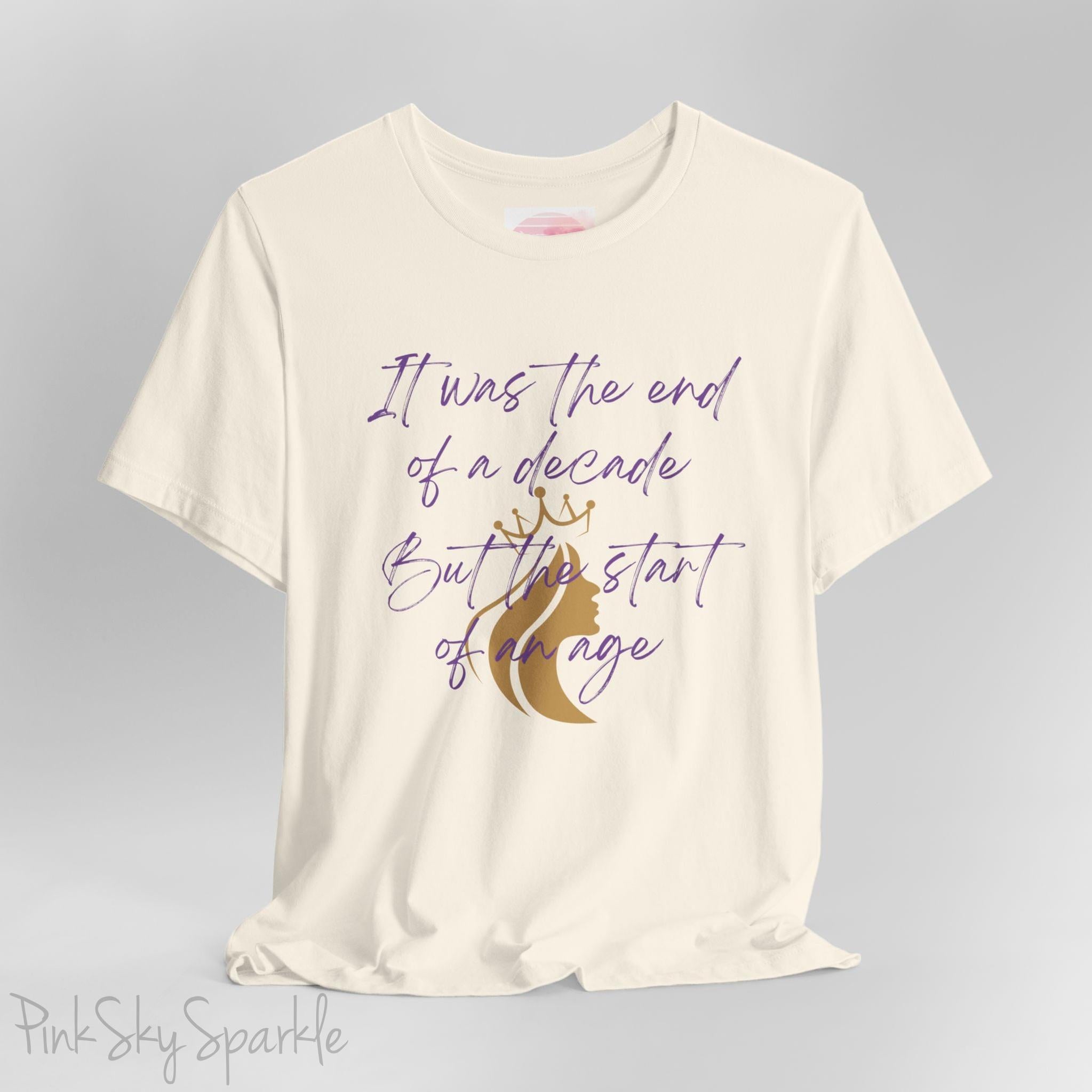 Embrace the excitement of a new era with our End of a Decade, Start of an Age T-shirt, inspired by Taylor Swift's iconic lyrics. Featuring the words It was the end of a decade, But the start of an age in a purple marker script font with a gold silhouette of a woman wearing a crown.