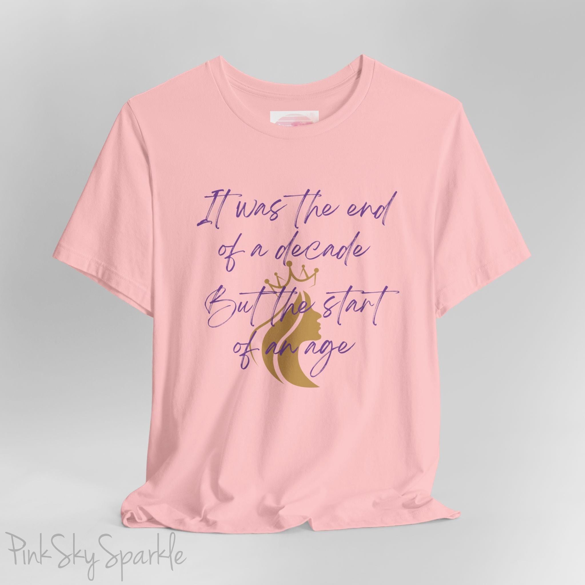 Embrace the excitement of a new era with our End of a Decade, Start of an Age T-shirt, inspired by Taylor Swift's iconic lyrics. Featuring the words It was the end of a decade, But the start of an age in a purple marker script font with a gold silhouette of a woman wearing a crown.