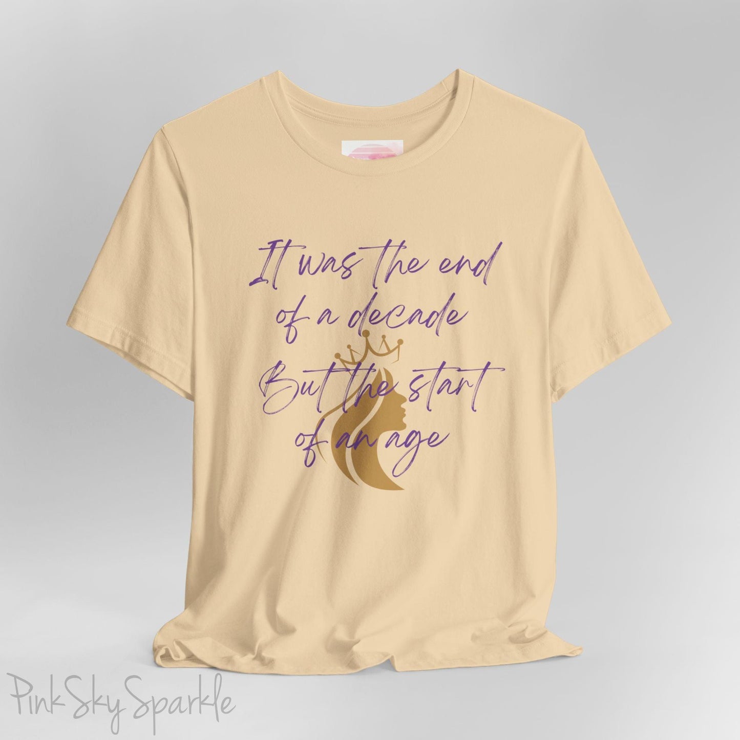 Embrace the excitement of a new era with our End of a Decade, Start of an Age T-shirt, inspired by Taylor Swift's iconic lyrics. Featuring the words It was the end of a decade, But the start of an age in a purple marker script font with a gold silhouette of a woman wearing a crown.