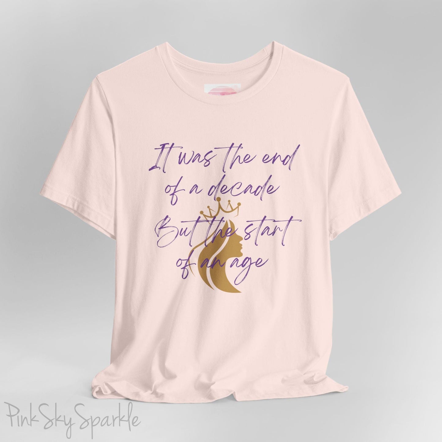 Embrace the excitement of a new era with our End of a Decade, Start of an Age T-shirt, inspired by Taylor Swift's iconic lyrics. Featuring the words It was the end of a decade, But the start of an age in a purple marker script font with a gold silhouette of a woman wearing a crown.