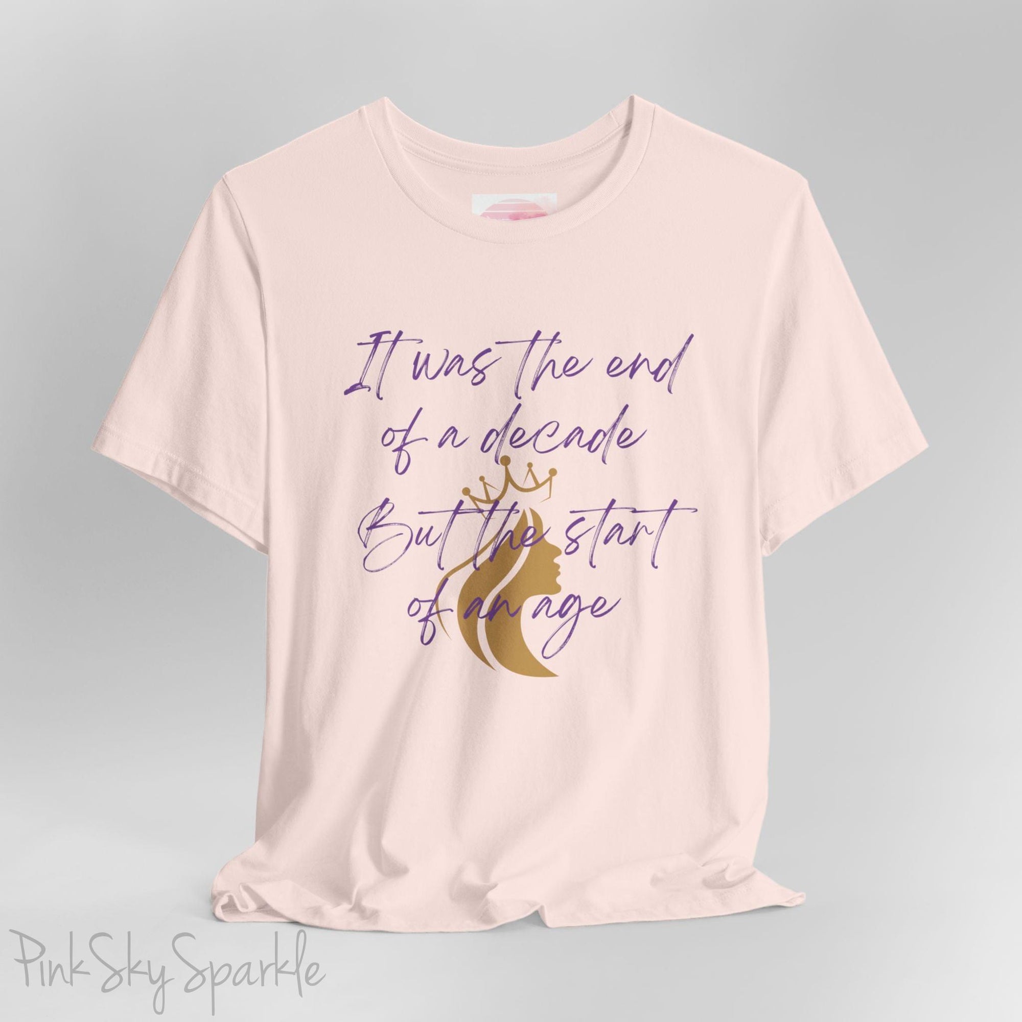 Embrace the excitement of a new era with our End of a Decade, Start of an Age T-shirt, inspired by Taylor Swift's iconic lyrics. Featuring the words It was the end of a decade, But the start of an age in a purple marker script font with a gold silhouette of a woman wearing a crown.