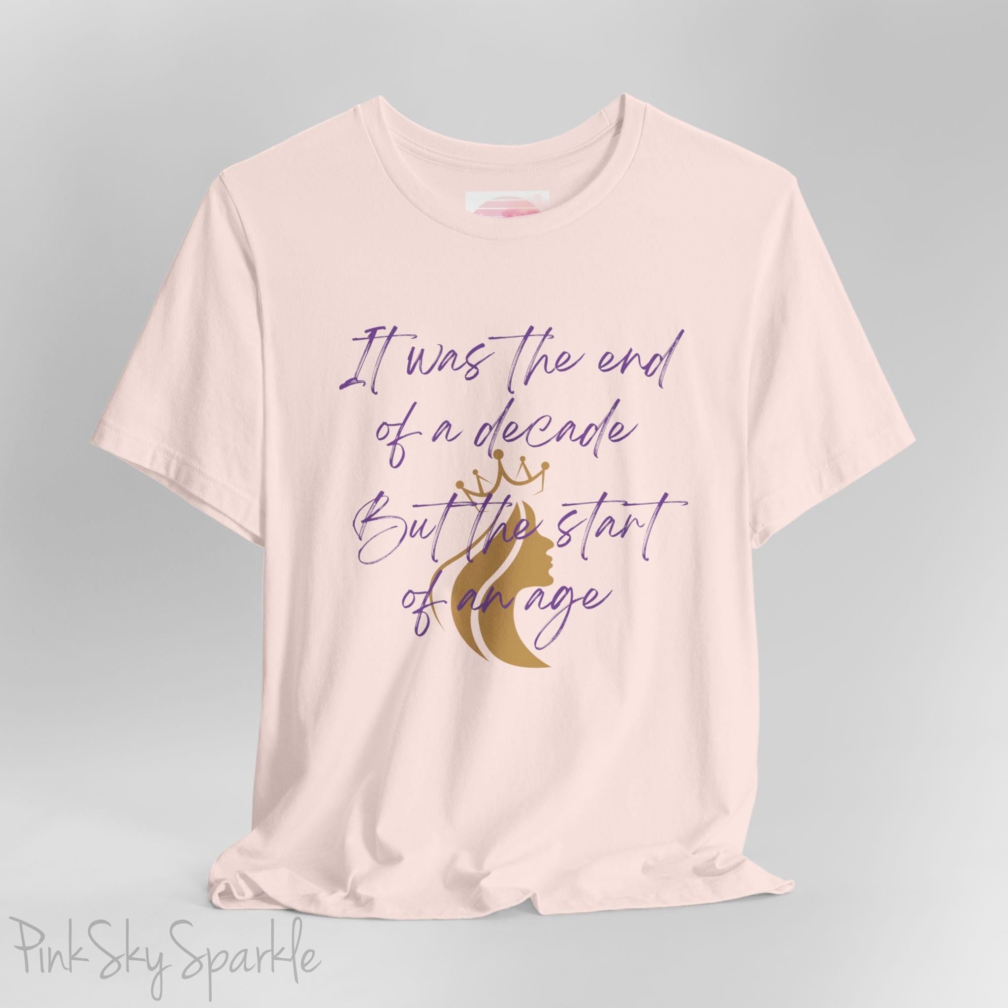 Embrace the excitement of a new era with our End of a Decade, Start of an Age T-shirt, inspired by Taylor Swift's iconic lyrics. Featuring the words It was the end of a decade, But the start of an age in a purple marker script font with a gold silhouette of a woman wearing a crown.