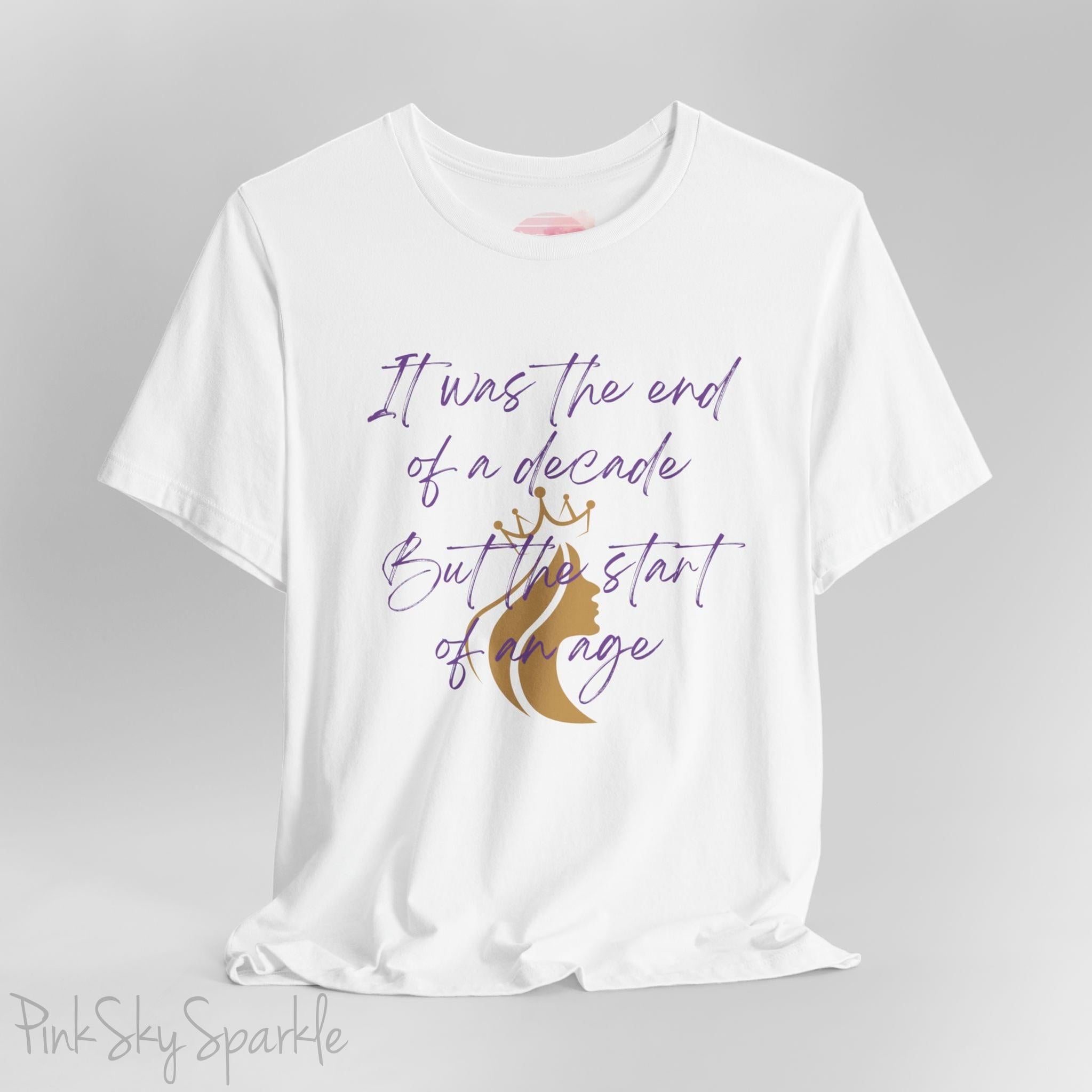 Embrace the excitement of a new era with our End of a Decade, Start of an Age T-shirt, inspired by Taylor Swift's iconic lyrics. Featuring the words It was the end of a decade, But the start of an age in a purple marker script font with a gold silhouette of a woman wearing a crown.