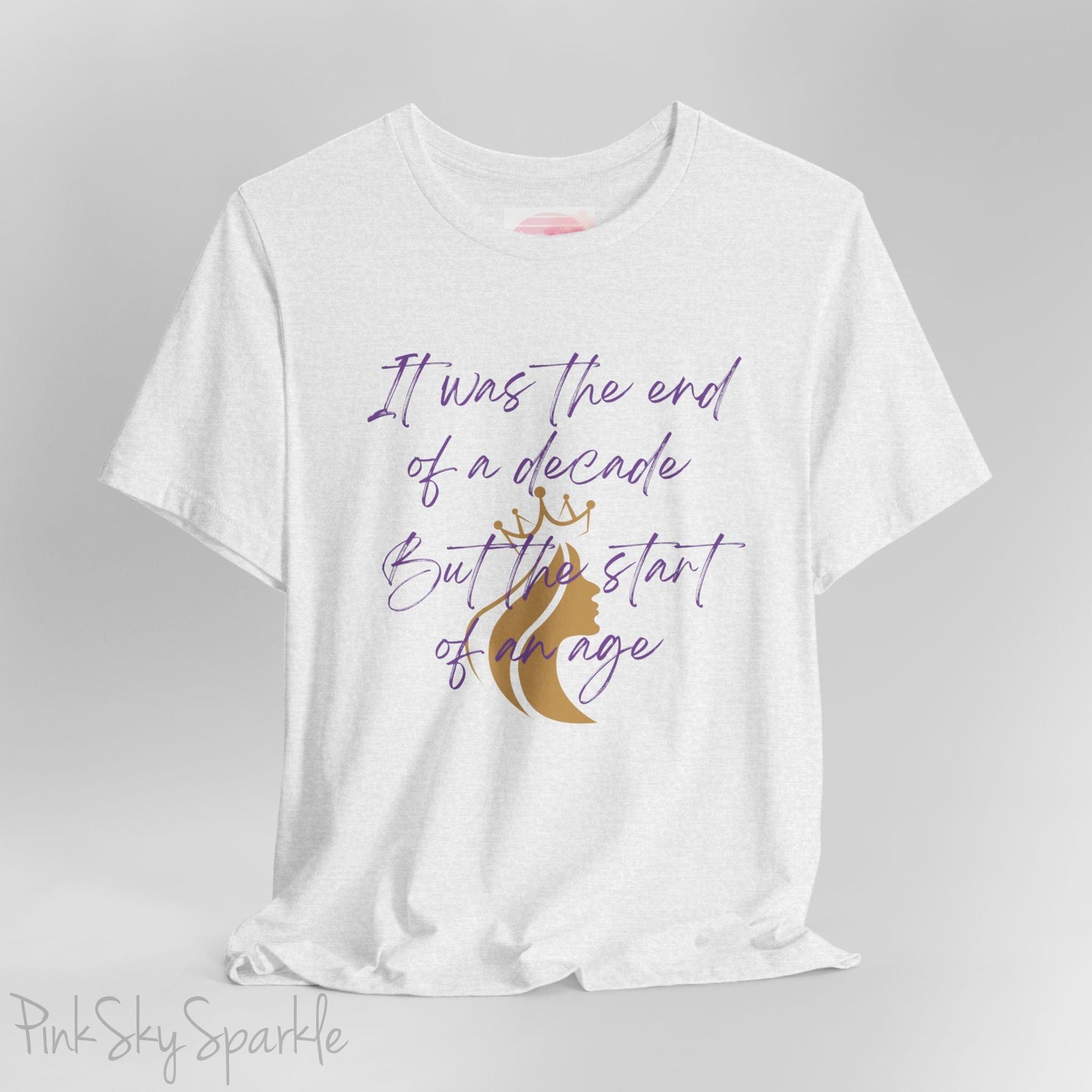 Embrace the excitement of a new era with our End of a Decade, Start of an Age T-shirt, inspired by Taylor Swift's iconic lyrics. Featuring the words It was the end of a decade, But the start of an age in a purple marker script font with a gold silhouette of a woman wearing a crown.