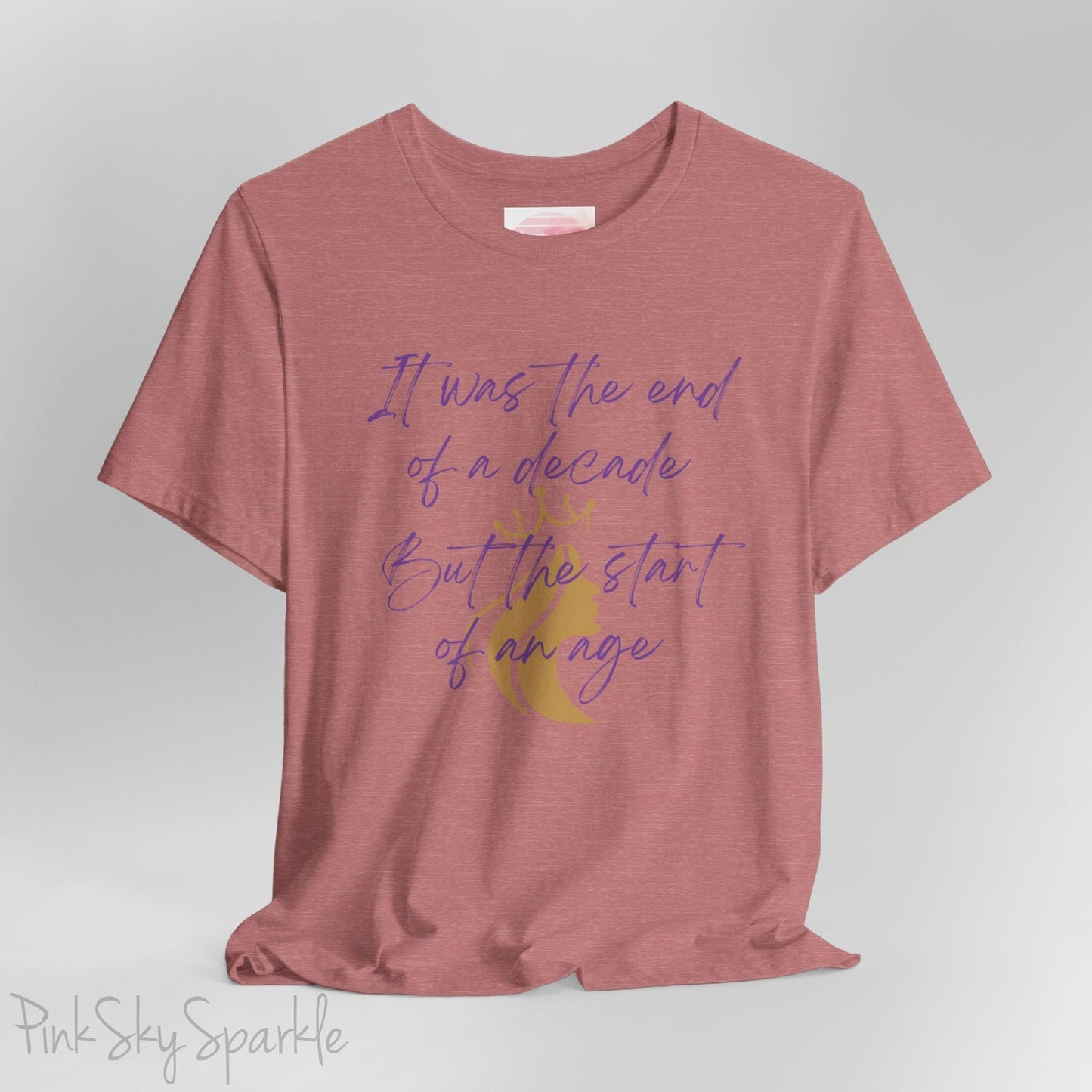 Embrace the excitement of a new era with our End of a Decade, Start of an Age T-shirt, inspired by Taylor Swift's iconic lyrics. Featuring the words It was the end of a decade, But the start of an age in a purple marker script font with a gold silhouette of a woman wearing a crown.