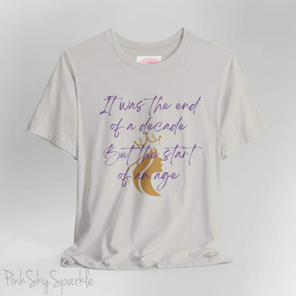 Embrace the excitement of a new era with our End of a Decade, Start of an Age T-shirt, inspired by Taylor Swift's iconic lyrics. Featuring the words It was the end of a decade, But the start of an age in a purple marker script font with a gold silhouette of a woman wearing a crown.