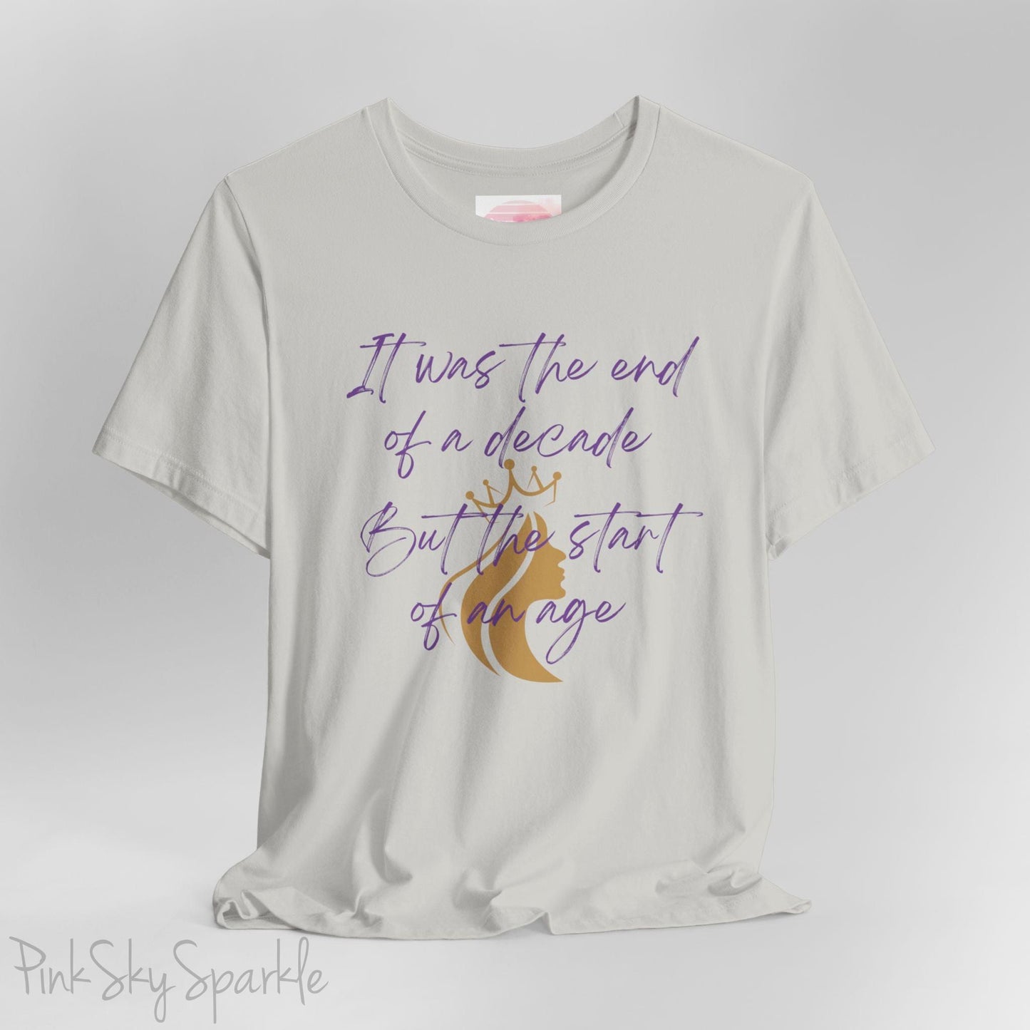 Embrace the excitement of a new era with our End of a Decade, Start of an Age T-shirt, inspired by Taylor Swift's iconic lyrics. Featuring the words It was the end of a decade, But the start of an age in a purple marker script font with a gold silhouette of a woman wearing a crown.