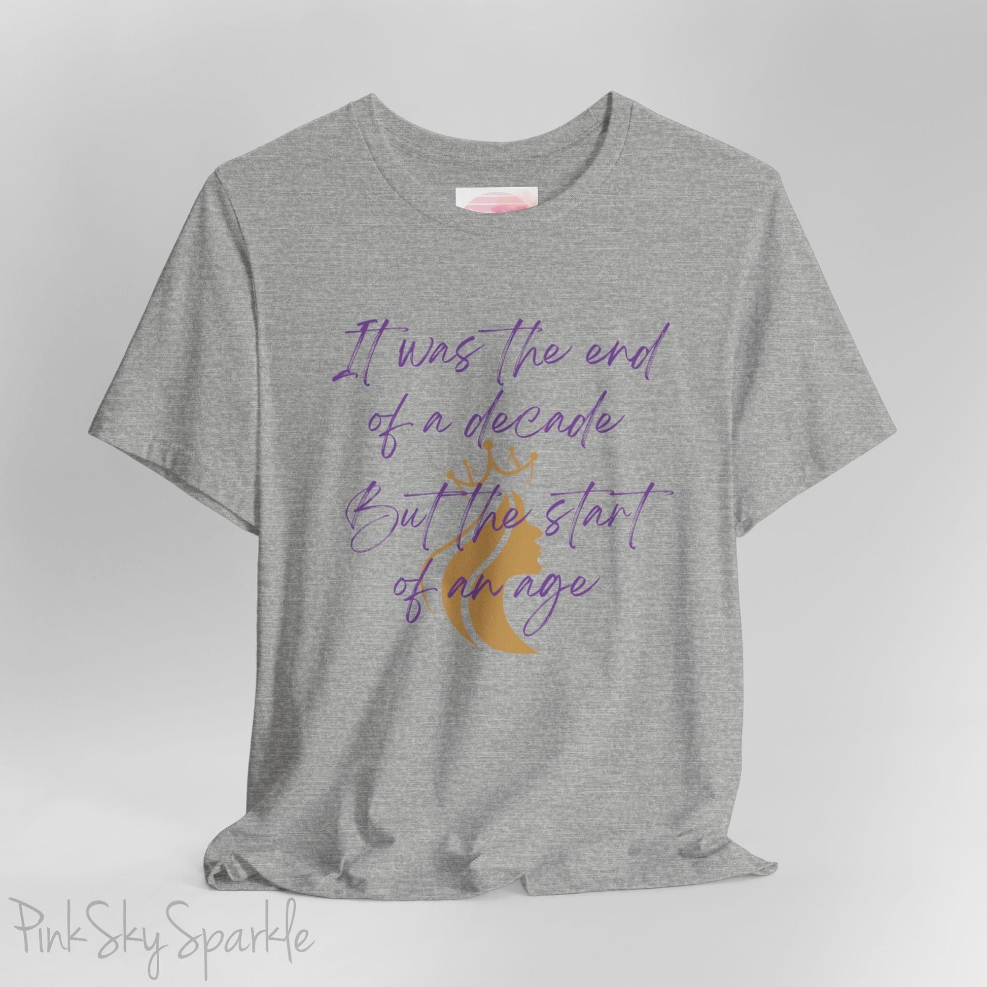 Embrace the excitement of a new era with our End of a Decade, Start of an Age T-shirt, inspired by Taylor Swift's iconic lyrics. Featuring the words It was the end of a decade, But the start of an age in a purple marker script font with a gold silhouette of a woman wearing a crown.