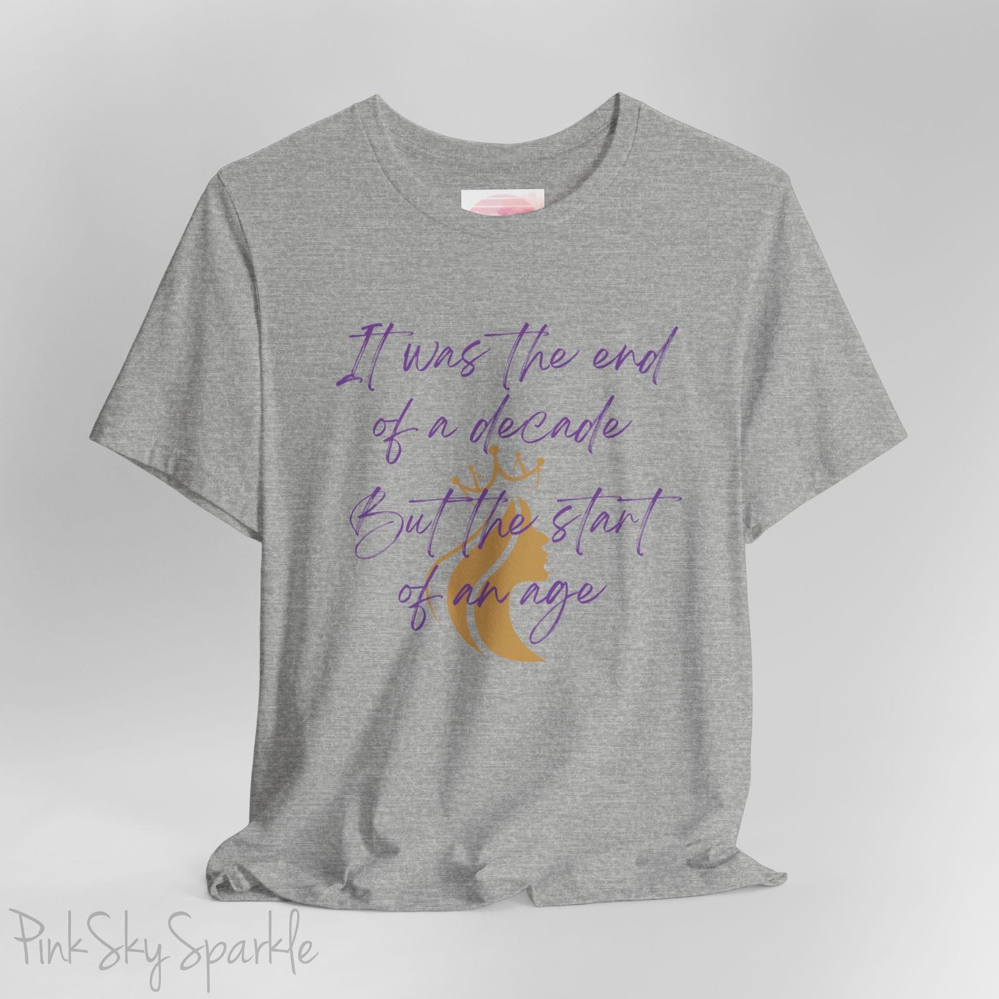 Embrace the excitement of a new era with our End of a Decade, Start of an Age T-shirt, inspired by Taylor Swift's iconic lyrics. Featuring the words It was the end of a decade, But the start of an age in a purple marker script font with a gold silhouette of a woman wearing a crown.