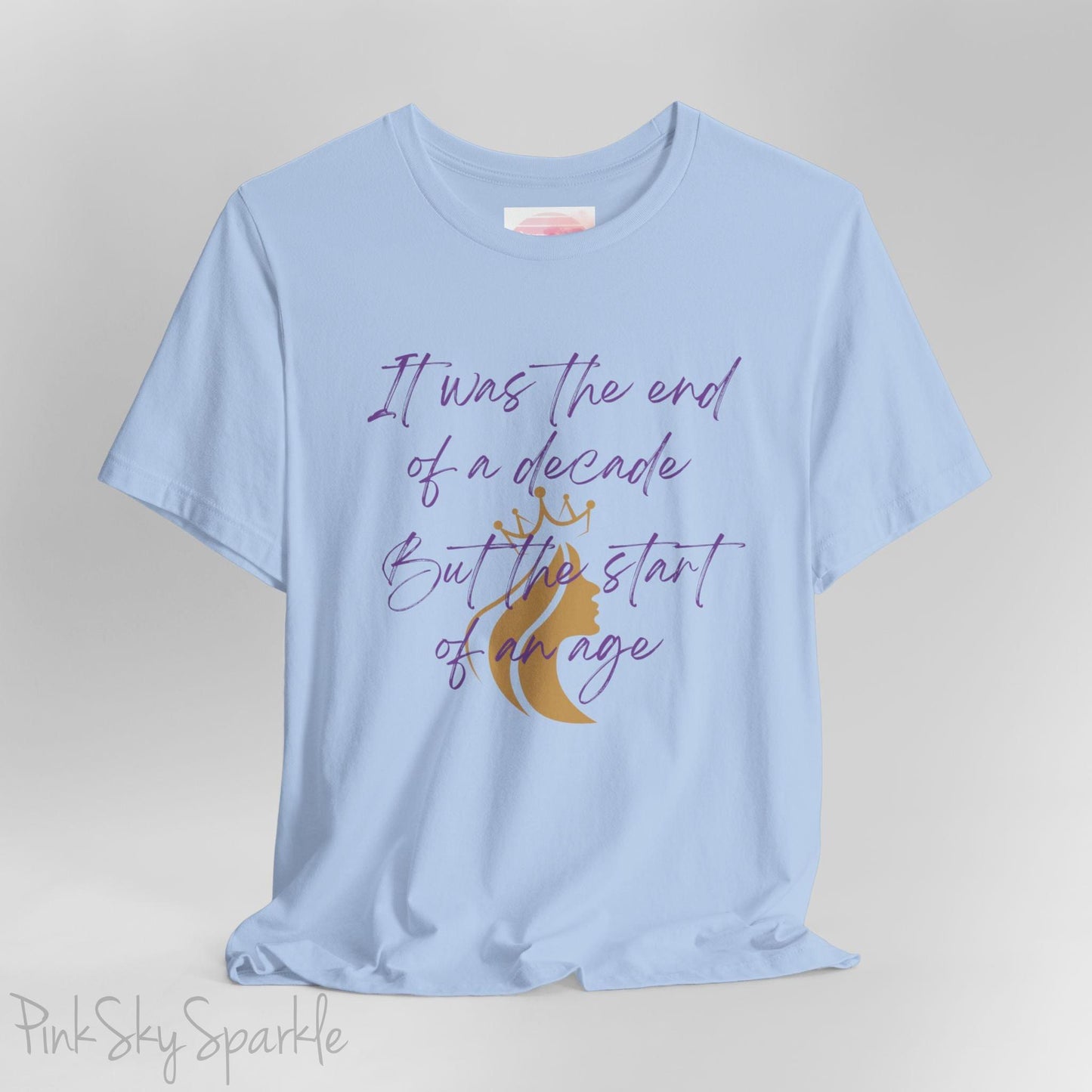 Embrace the excitement of a new era with our End of a Decade, Start of an Age T-shirt, inspired by Taylor Swift's iconic lyrics. Featuring the words It was the end of a decade, But the start of an age in a purple marker script font with a gold silhouette of a woman wearing a crown.
