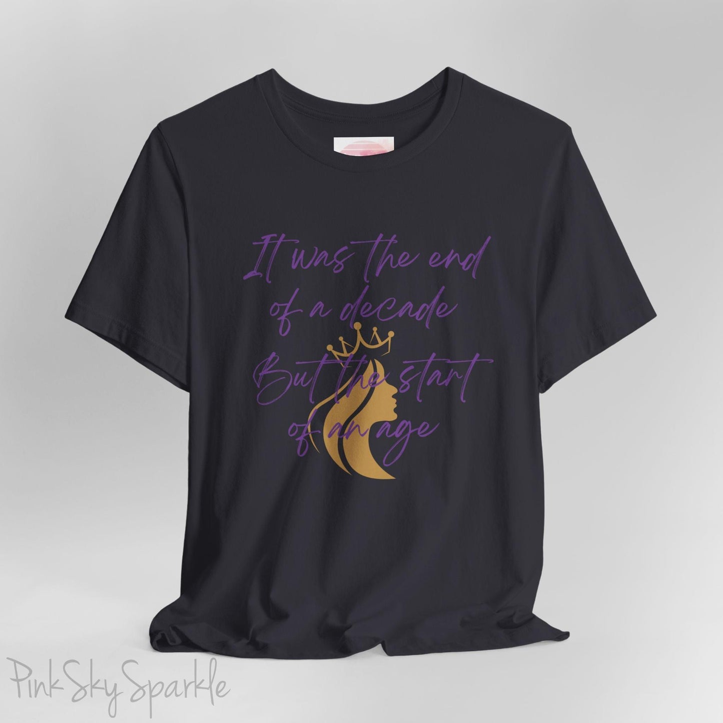 Embrace the excitement of a new era with our End of a Decade, Start of an Age T-shirt, inspired by Taylor Swift's iconic lyrics. Featuring the words It was the end of a decade, But the start of an age in a purple marker script font with a gold silhouette of a woman wearing a crown.