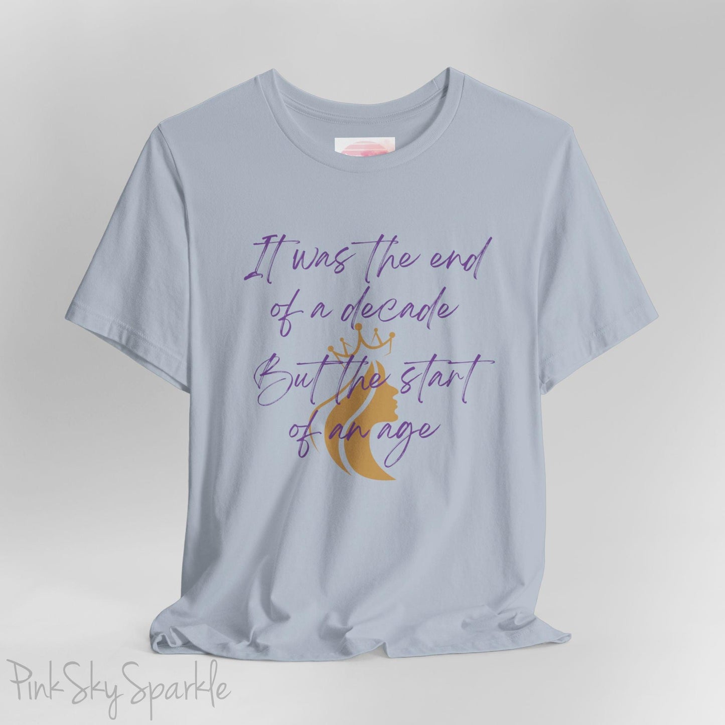 Embrace the excitement of a new era with our End of a Decade, Start of an Age T-shirt, inspired by Taylor Swift's iconic lyrics. Featuring the words It was the end of a decade, But the start of an age in a purple marker script font with a gold silhouette of a woman wearing a crown.