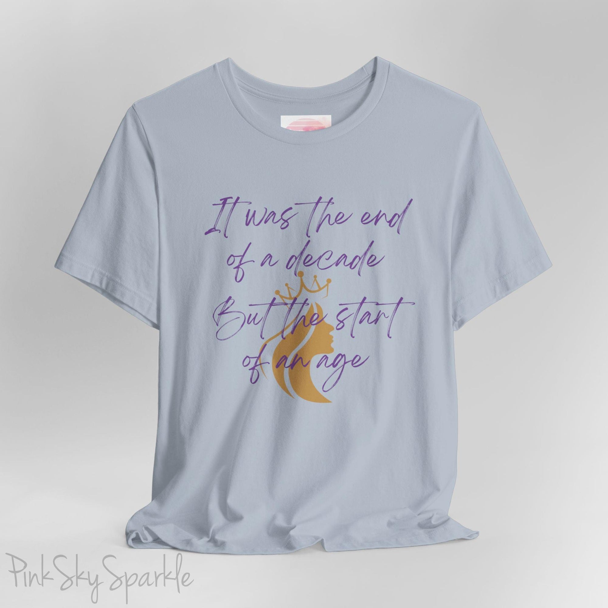 Embrace the excitement of a new era with our End of a Decade, Start of an Age T-shirt, inspired by Taylor Swift's iconic lyrics. Featuring the words It was the end of a decade, But the start of an age in a purple marker script font with a gold silhouette of a woman wearing a crown.