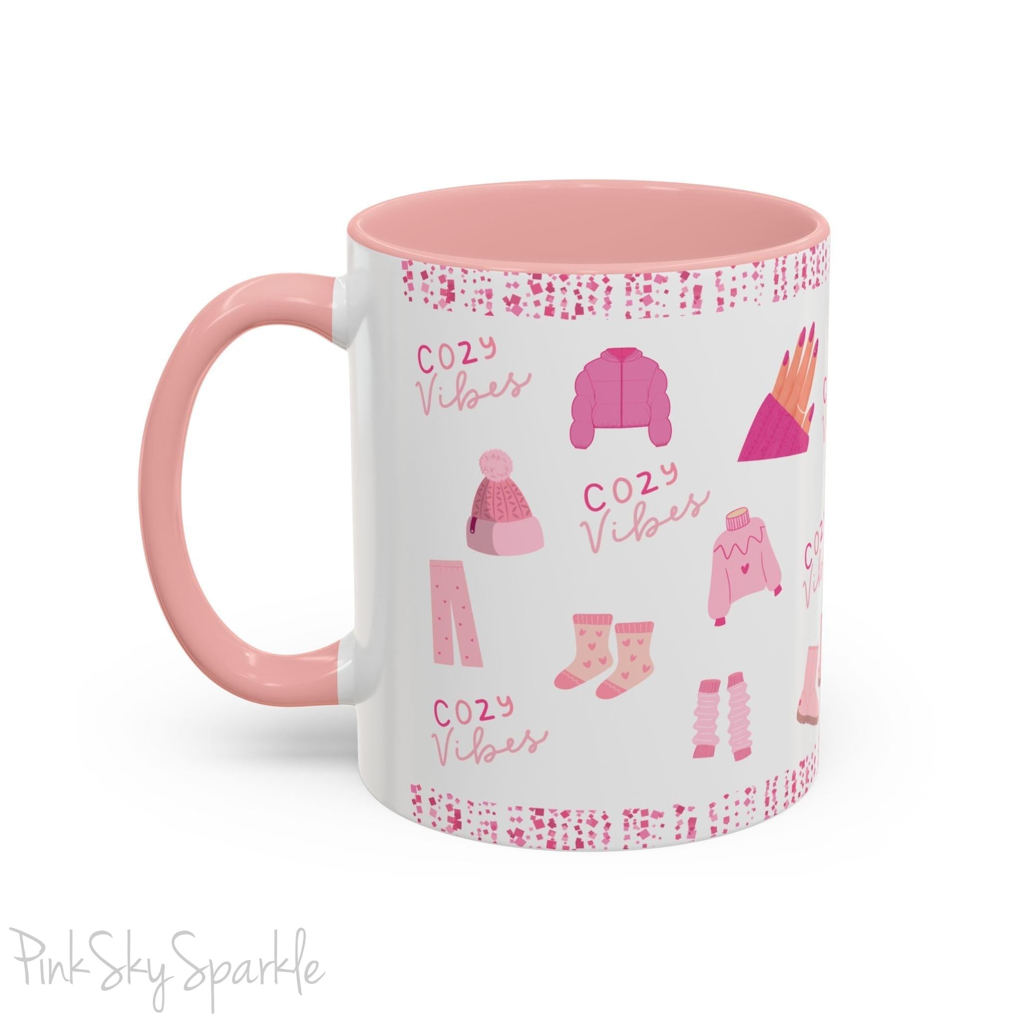 Pink Cozy Vibes Mug - Perfect for coffee, tea, or hot cocoa lovers! This ceramic mug features 'cozy vibes' in a pink font, surrounded by cute illustrations of pink cozy items such as slippers, mittens, blankets and candles. Ideal for creating a warm, cozy atmosphere, this pink-handled mug (also available in light blue, black and navy) makes a great gift for anyone who loves comfort, style and the color pink.