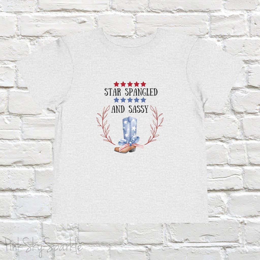 Dress your little one in patriotic style with our adorable toddler t-shirt, perfect for the 4th of July! This charming tee features the playful phrase "Star Spangled and Sassy" alongside a cute graphic of a red, white, and blue cowgirl boot adorned with a bow.