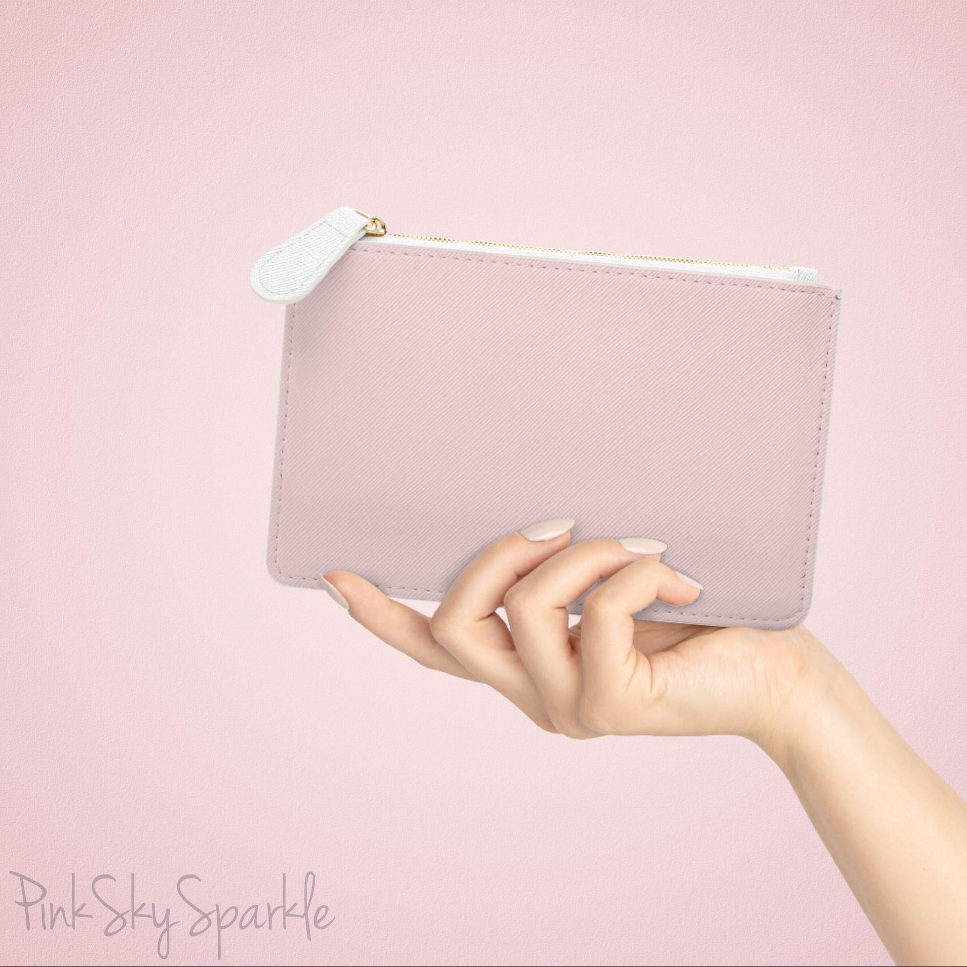 Hand holding the plain pink back of the mini clutch bag against a soft pink background.