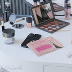 Pink mini clutch bag shown on a vanity surrounded by makeup products.