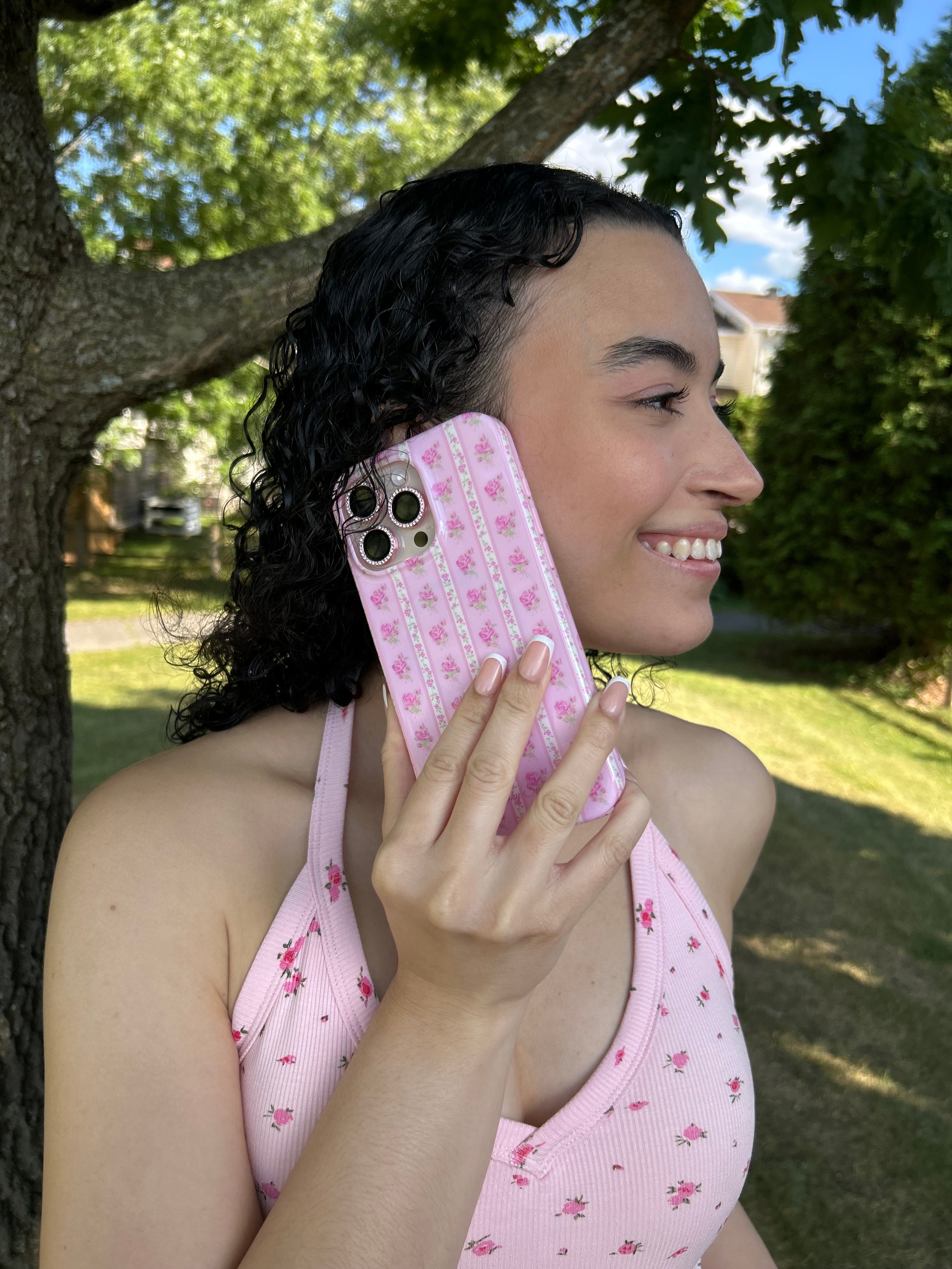 Woman under a tree holding an iPhone 16 Pro Max phone with a pink floral phone case