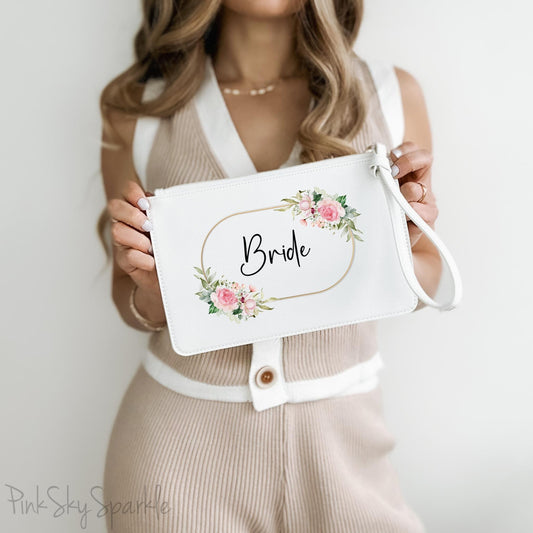 White clutch wristlet bag with a gold, pink and green floral design and the word Bride in a fancy font black font in the centre. 