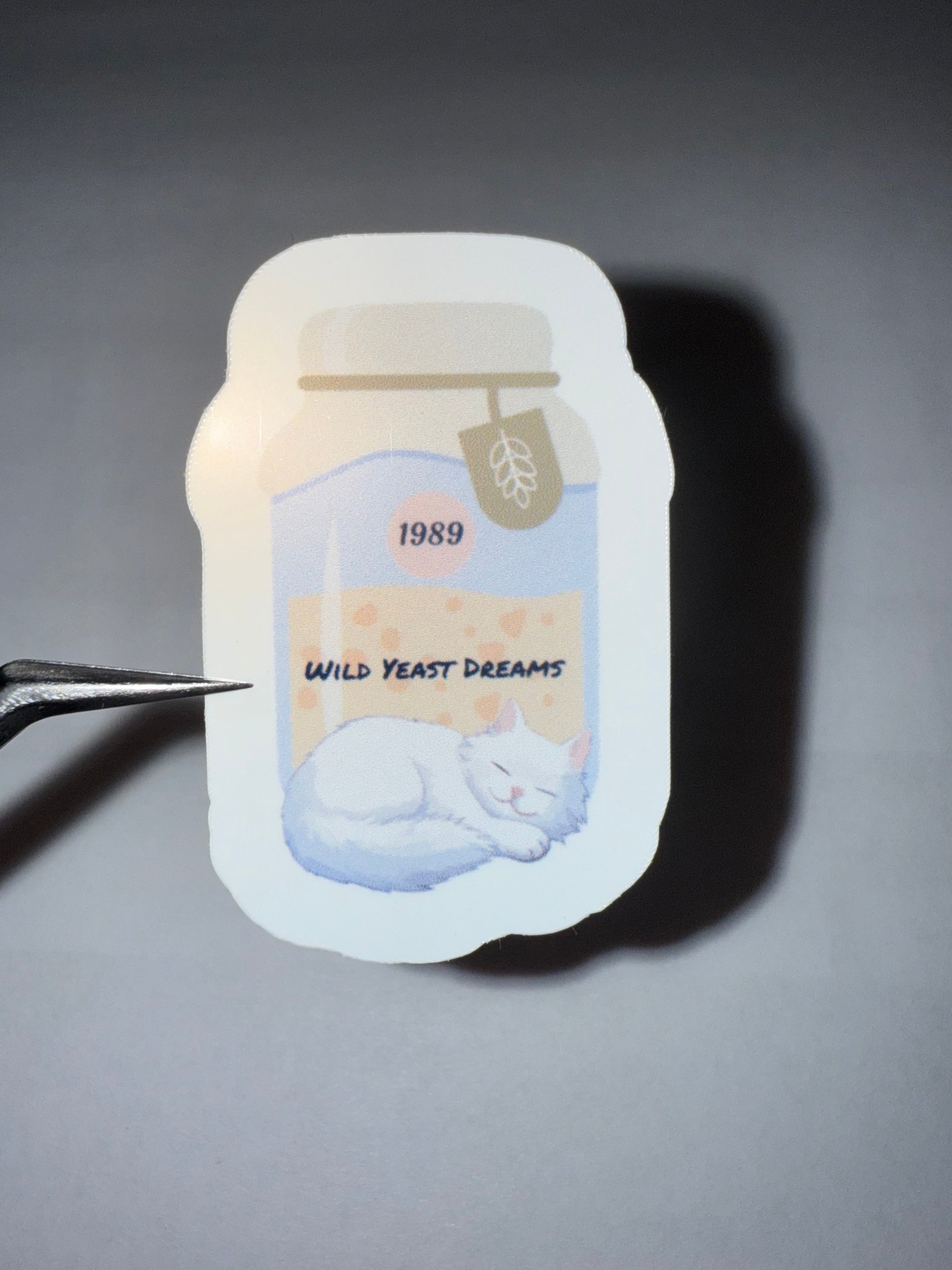 Sticker featuring a jar of sourdough starter and a sleeping white cat with the pun "Wild Yeast Dreams" 