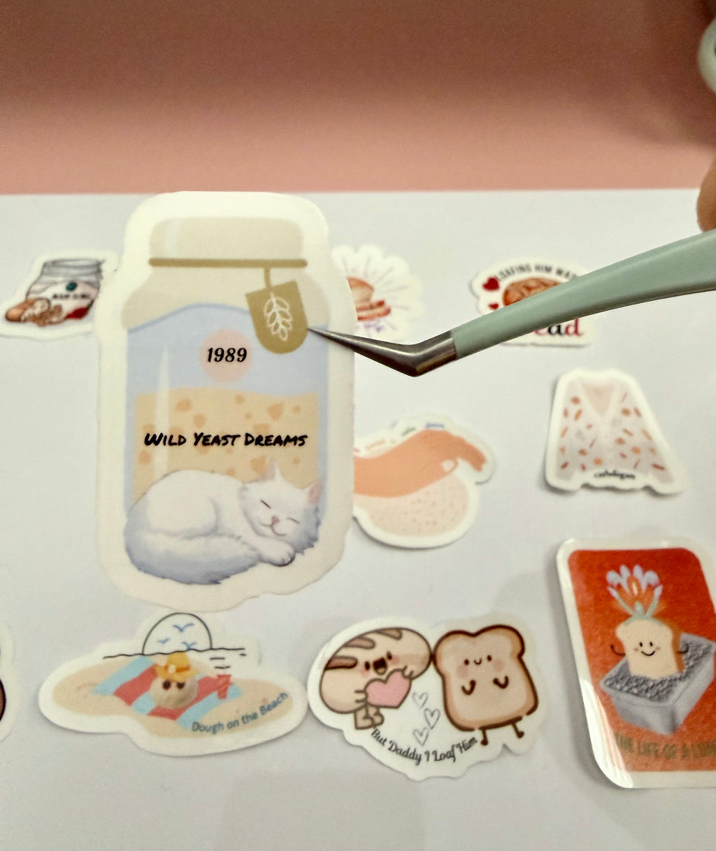 A sticker with a white cat sleeping in front of a sourdough starter jar that says 'wild yeast dreams 1989' on it.