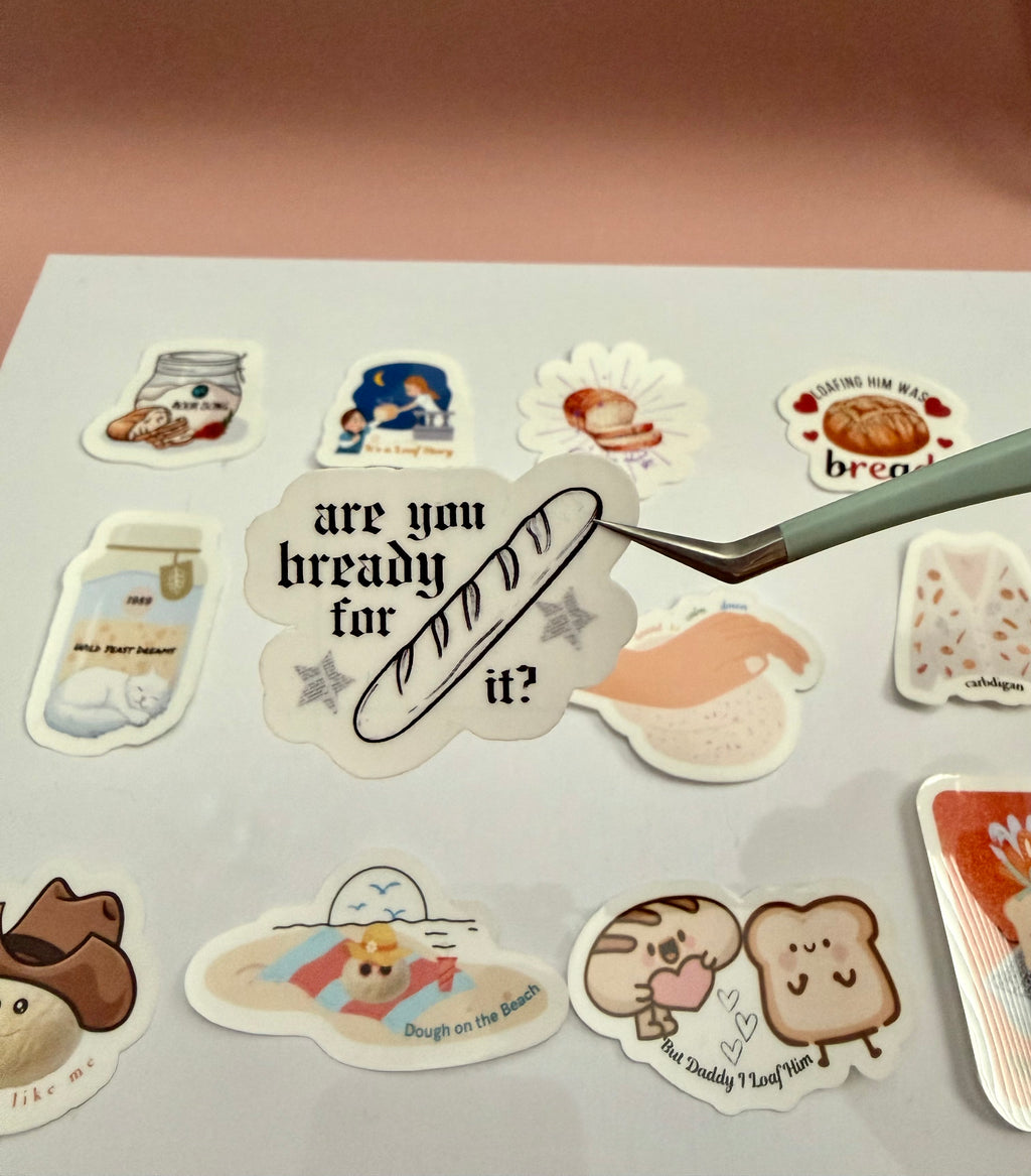 Sticker with a baguette and stars with newspaper print design that says 'are you bready for it?' 